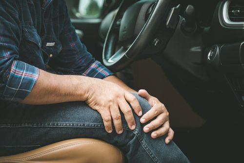 Image is of a man holding his knee in pain due to long hour driving concept of knee pain treatment in Chicago