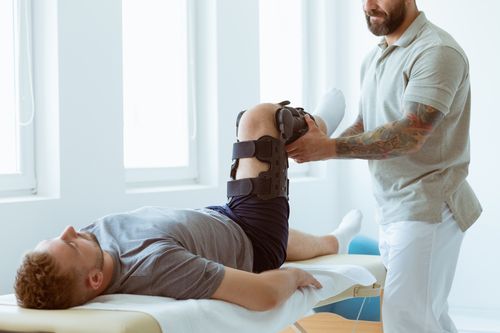 Image is of a male patient with a knee brace laying on a table being treated by a physical therapist concept of slip and fall injury treatment in Chicago