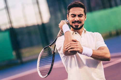 Image is of a male tennis player holding his elbow concept of elbow pain treatment in Chicago