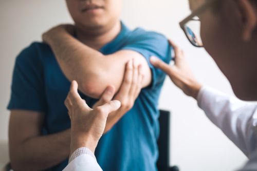 Image is of a doctor assessing a patient's elbow, concept of elbow pain treatment in Chicago