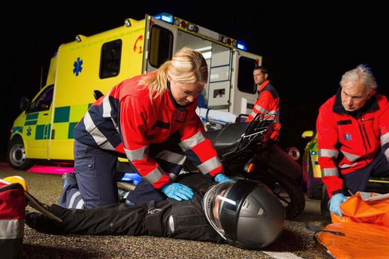 Image is of a paramedic attending to a motorcycle driver laying on the ground following a motorcycle accident, concept of understanding concussions and head injuries after a motorcycle accident