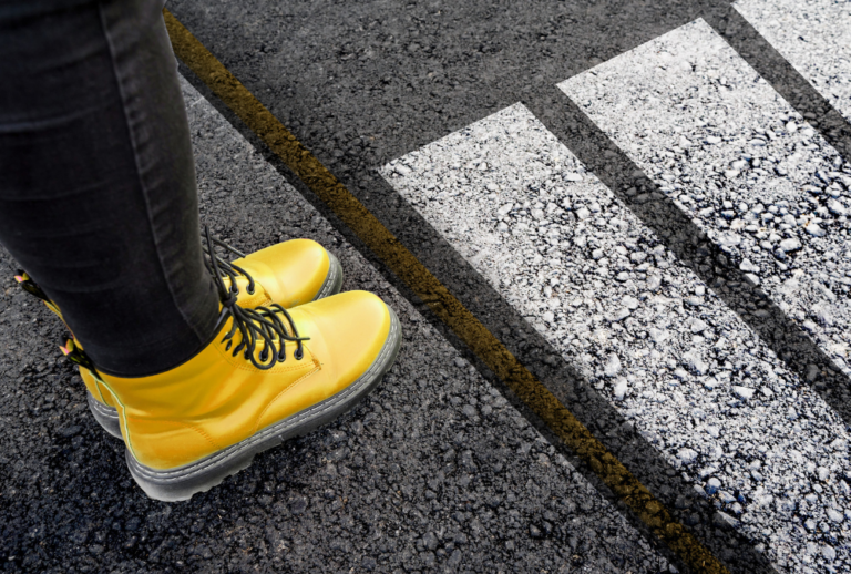 Image is of a woman wearing black jeans, and bright yellow boots about to step into a crosswalk, concept of pedestrian accident injury treatment options