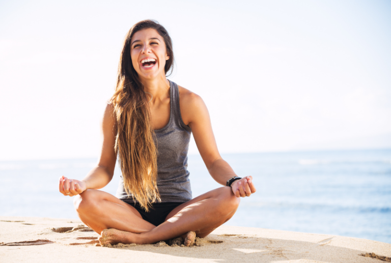 Image is of a smiling woman sitting on the beach, concept of 6 types of injections for accident pain relief