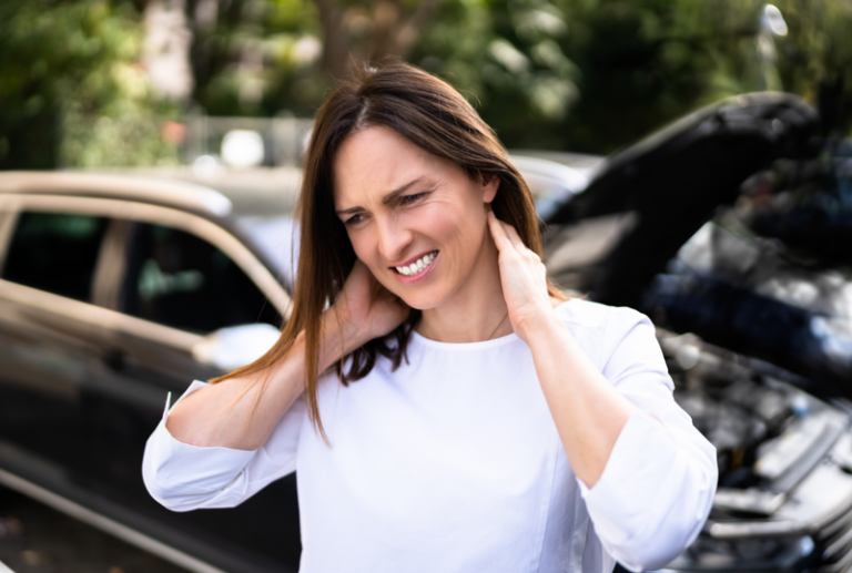 Image is of a woman in pain and holding her neck after a car accident