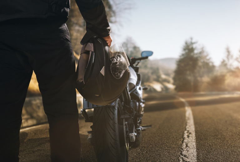 Image is of a closeup of a motorcycle rider standing behind motorcycle, concept of motorcycle accident injuries