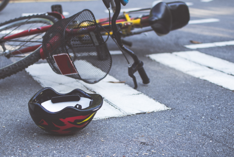 Image is of a bicycle and bicycle helmet laying on the ground in a road, concept of common bicycle accident injuries and how to recover