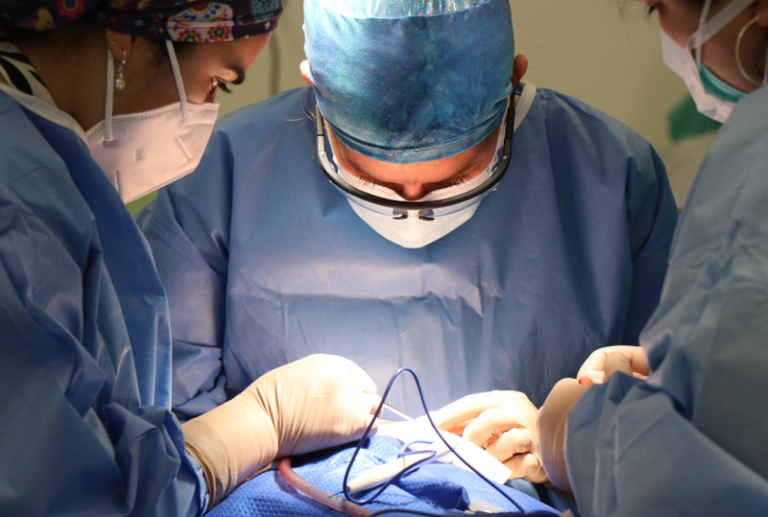 Image is of a surgeon and team performing a surgery on a patient