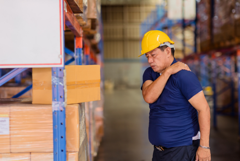 Image is of a man in a warehouse gripping his shoulder in pain, concept of what to do after being injured on the job