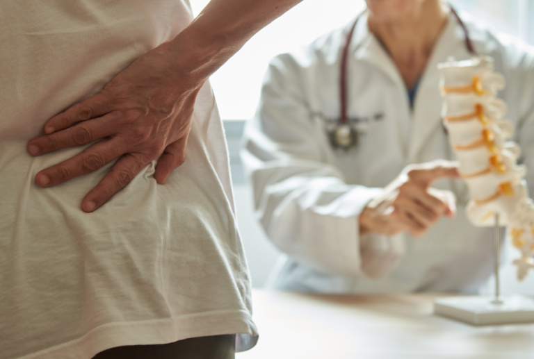 Image is of a doctor showing a patient about the spine while the patient is hold their back in pain, concept of questions to ask your doctor after a personal injury